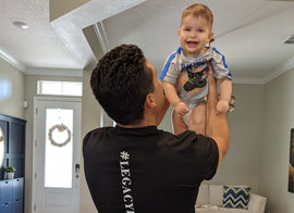 Miguel holding up his youngest son over his head while they both smile.