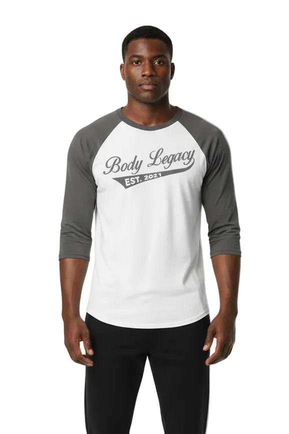 A man modeling a white and gray raglan baseball t-shirt with 'Body Legacy EST. 2021 printed on the chest, paired with black pants, against a plain white background.