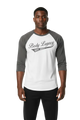 A man modeling a white and gray raglan baseball t-shirt with 'Body Legacy EST. 2021 printed on the chest, paired with black pants, against a plain white background.